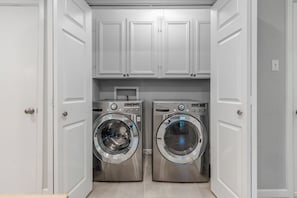 Una sala de lavandería con dos lavadoras de acero inoxidable y almacenamiento superior con armarios blancos.