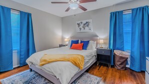 Een slaapkamer met een bed, nachtkastje, lamp, wereldkaart aan de muur en plafondventilator.