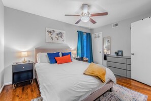 Un dormitorio con cama, mesitas de noche, cómoda, ventilador de techo y un mapa del mundo en la pared.
