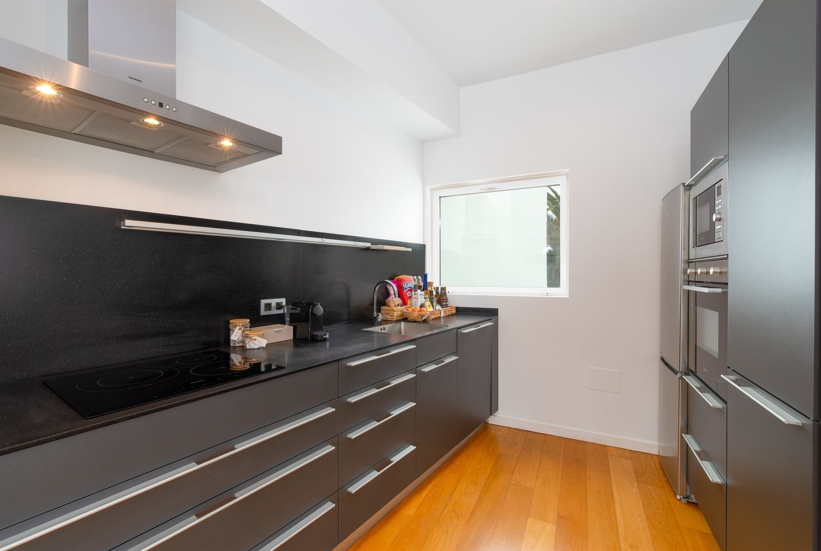 Una cocina moderna con encimera negra, electrodomésticos de acero inoxidable y una ventana que proporciona luz natural.