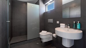 Une salle de bain moderne avec une douche à parois de verre, des toilettes, un lavabo avec un miroir et des articles de toilette.