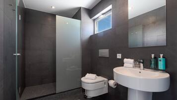 Un baño moderno con cabina de ducha de vidrio, inodoro, lavabo con espejo y artículos de aseo.