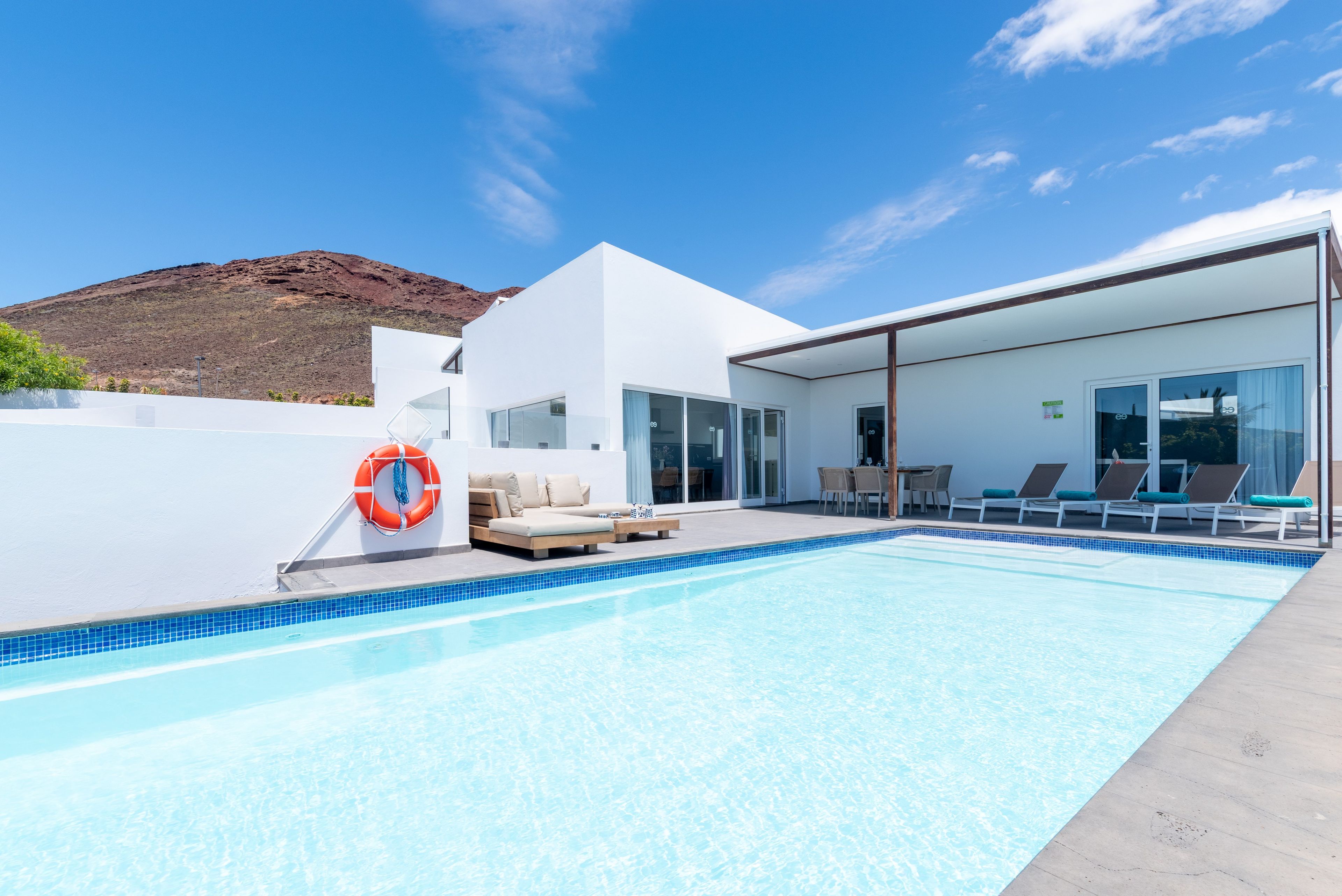 Zona de piscina moderna con cielo azul despejado, un flotador salvavidas y sillas de descanso.
