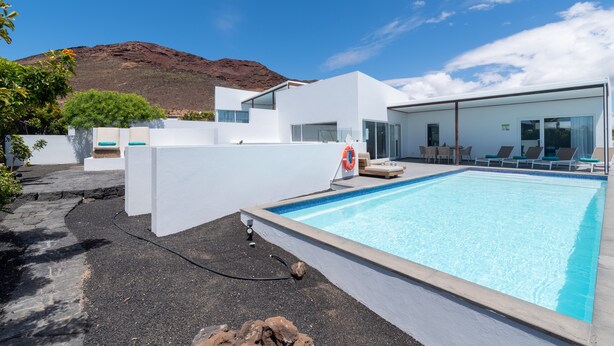 Un espace piscine moderne avec une piscine à l’eau d’un bleu limpide, des murs blancs et une montagne en arrière-plan.