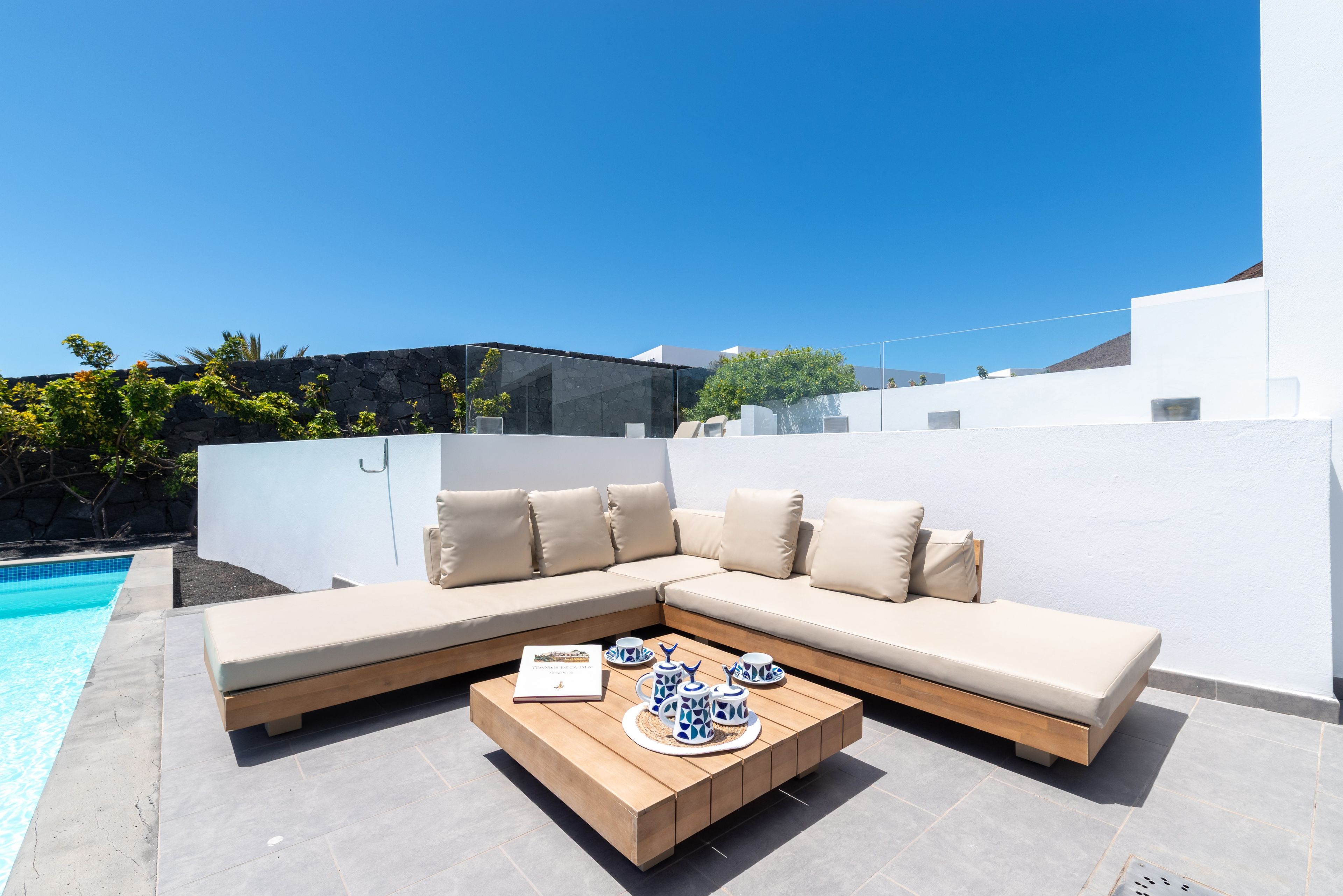 Un espacio exterior moderno con piscina, una mesa de centro de madera y un sofá seccional color beige.