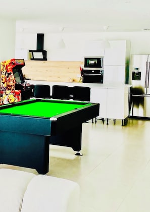 A pool table in a modern room with a kitchen area in the background.