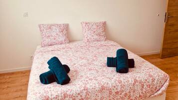 A single bed with a floral bedspread, two pillows, and two rolled-up towels.