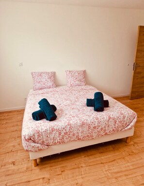 A single bed with a floral bedspread, two pillows, and two rolled-up towels.