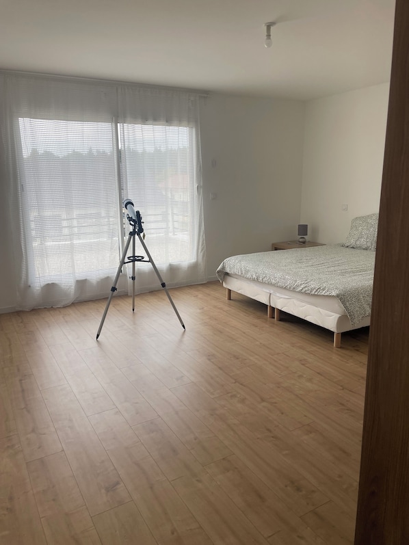 A bedroom with a bed, a nightstand, a lamp, and a telescope on a tripod.