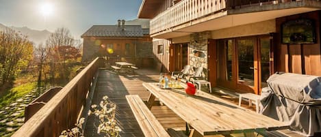 A wooden deck with outdoor seating, a barbecue grill, and a mountain backdrop.