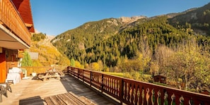 A wooden deck with outdoor furniture, overlooking a mountainous landscape with dense forests. - Terrace, fireplace or stove, tv, 100m², Champagny-en-Vanoise (Champagny-en-Vanoise)