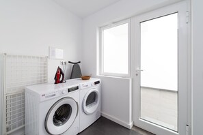 A laundry room with two front-loading washing machines, a drying rack, an ironing board, and a basket. - Vacation Villa 'Ereza Royal Deluxe Hoopoe 104' with Mountain View, Private Pool and Wi-Fi (Playa Blanca)