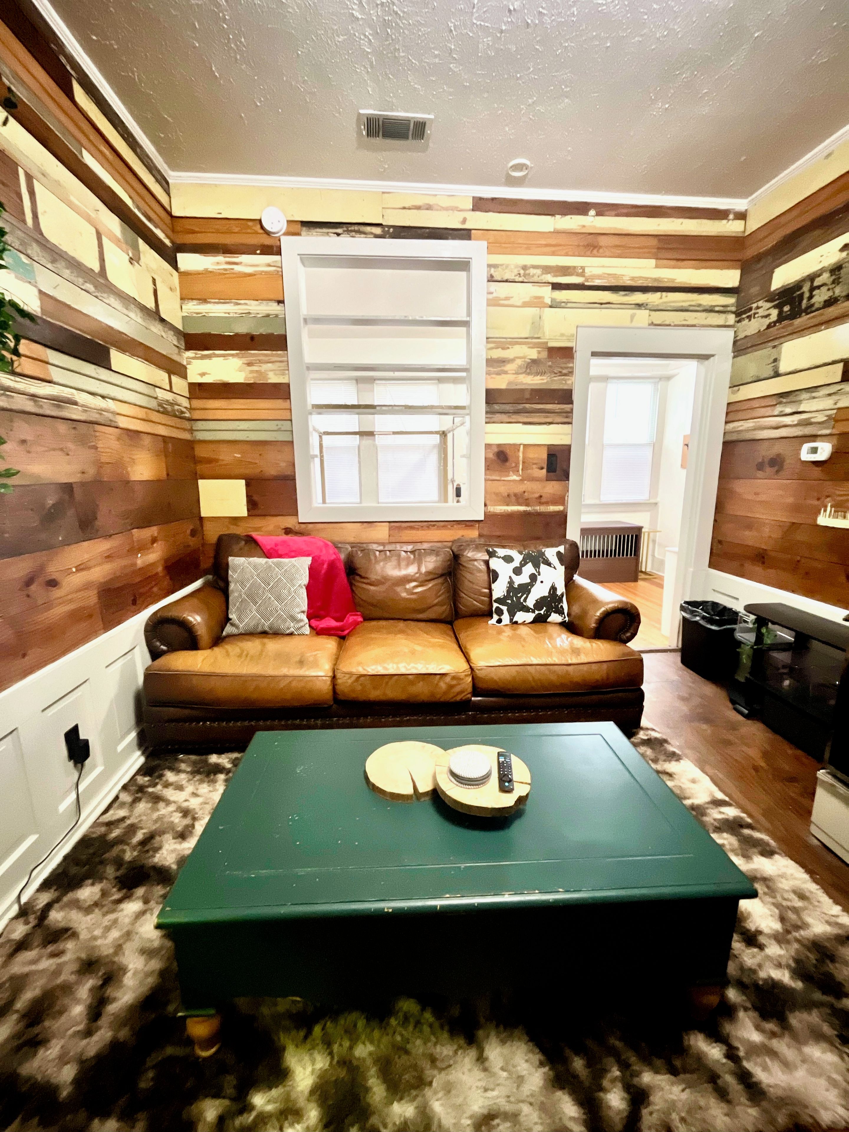 A cozy living room with a brown leather sofa, a green coffee table, and a wooden wall paneling.