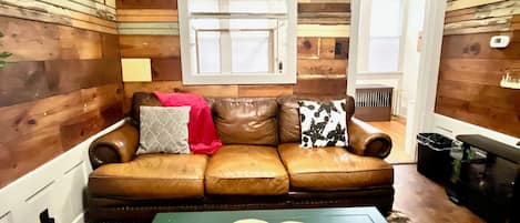 Un salon chaleureux avec un canapé en cuir marron, une table basse verte et un lambris en bois.