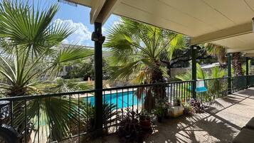 A covered outdoor area with a pool, palm trees, and a view of a building in the background.