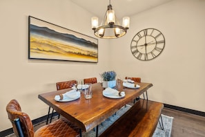 A dining area with a wooden table, leather chairs, a chandelier, a large painting, and a wall clock. - NEW! The Alders - Walk 2 Ski, Hot Tub, Fireplace (Dillon)