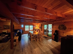 A cozy cabin interior with a dining area, wooden walls, and a large window.