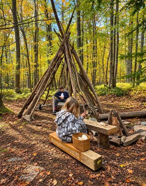 A forest scene with a wooden structure, a bench, and a table with a basket. - Cozy Deep Creek Log Cabin - Hot Tub, Firepit & Dock Slip (Oakland)