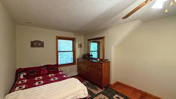 A bedroom with a bed, dresser, two windows, and a ceiling fan.