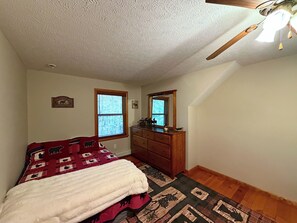 A bedroom with a bed, dresser, two windows, and a ceiling fan.
