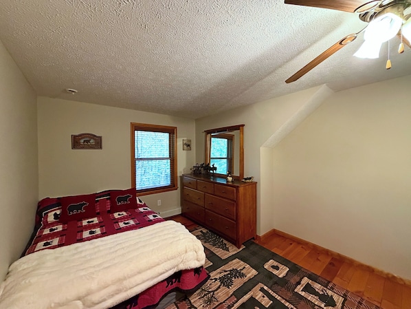 A bedroom with a bed, dresser, two windows, and a ceiling fan.