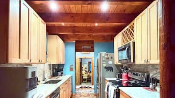 A kitchen with wooden cabinets, a refrigerator, a microwave, and a patterned rug.