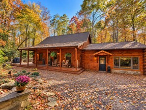 A log cabin with a porch, outdoor seating, and a stone pathway. - Cozy Deep Creek Log Cabin - Hot Tub, Firepit & Dock Slip (Oakland)