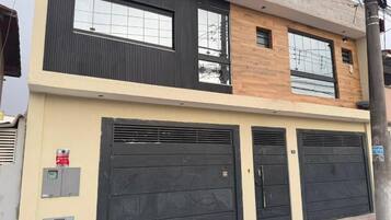 Un edificio de dos pisos con diseño moderno, que cuenta con grandes ventanales y un garaje con dos puertas negras.
