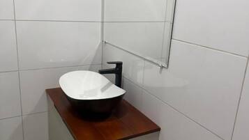 Un baño con lavamanos blanco, un espejo y un toallero negro.