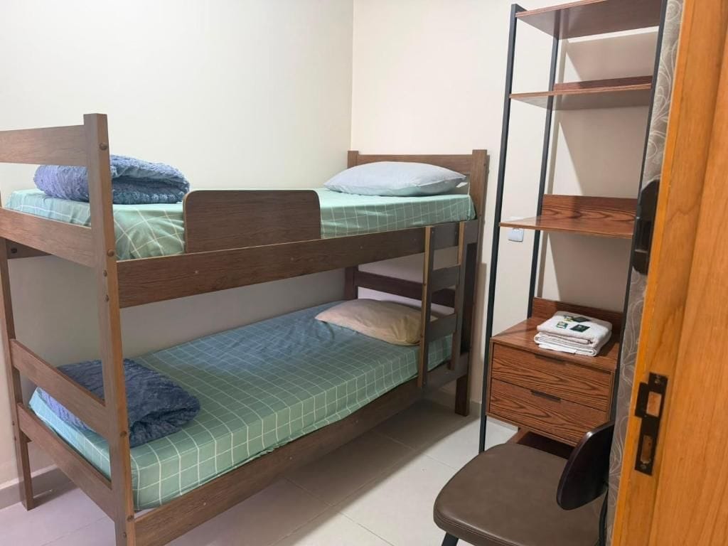 Una cama litera con escritorio y silla, una estantería y un armario pequeño.