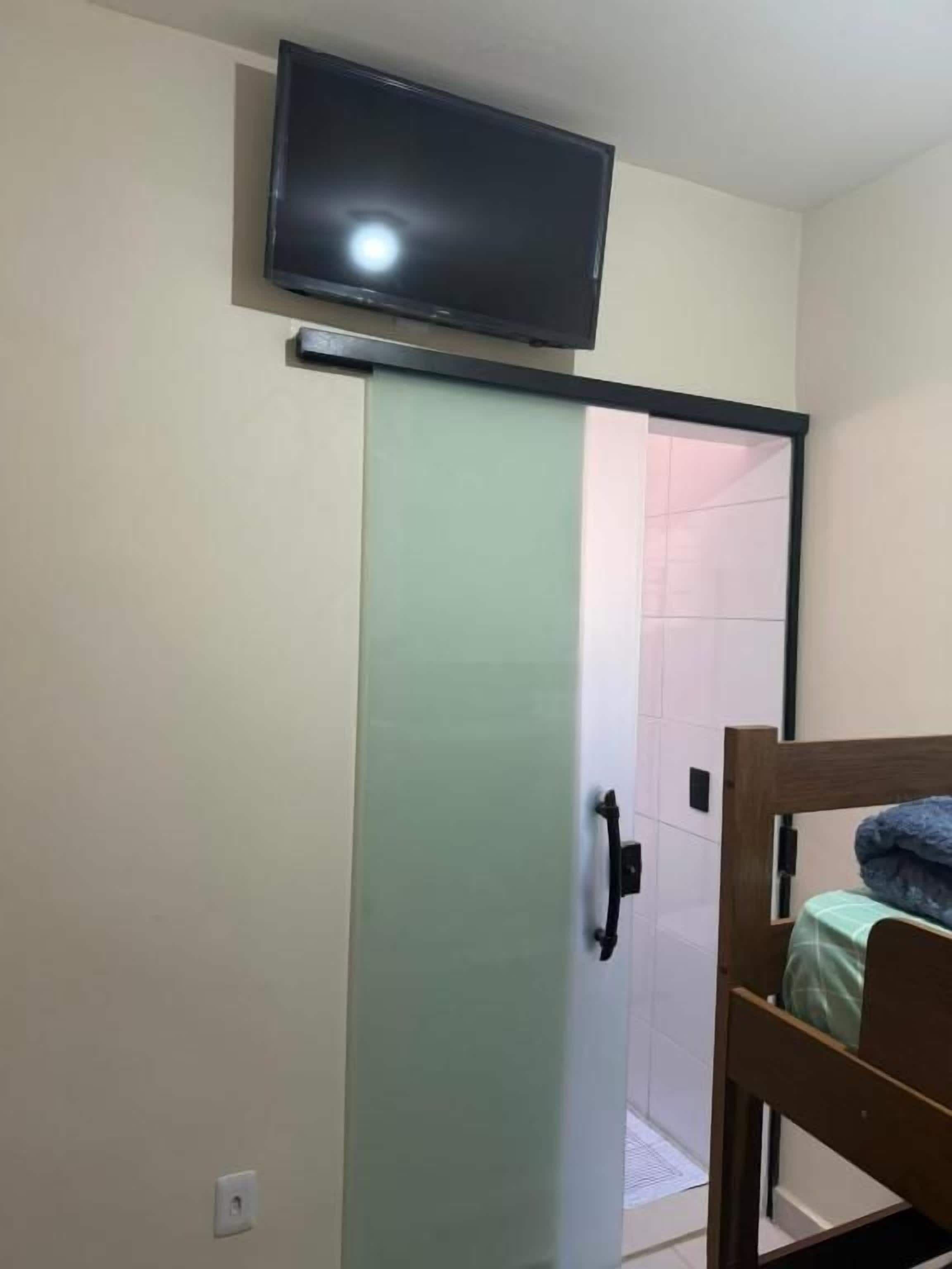 A room with a sliding door, a bed, a television mounted above the door, and a shower area.