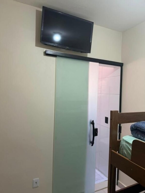 A room with a sliding door, a bed, a television mounted above the door, and a shower area.