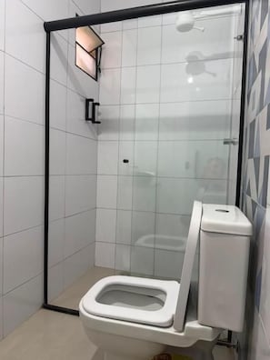 A modern bathroom with a glass shower enclosure, a toilet, and a wall-mounted light fixture. - Pousada SMART AIRPORT 10min (Guarulhos)
