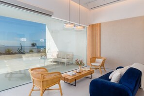 A modern living room with a glass wall, a blue sofa, wicker chairs, and a wooden coffee table. - Vacation Villa 'Ereza Royal Deluxe Hoopoe 101' with Mountain View, Wi-Fi and Air Conditioning (Playa Blanca)