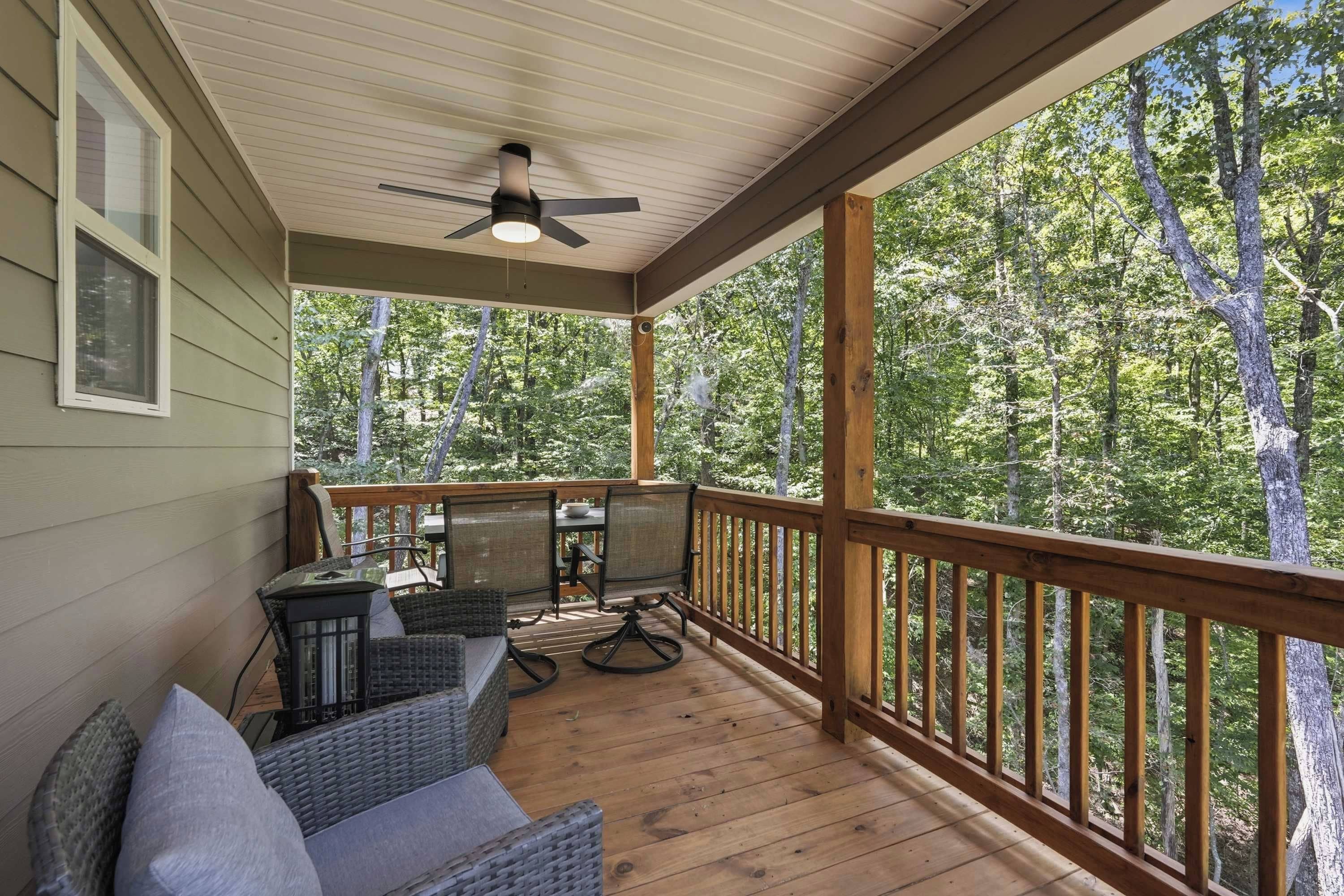 A covered porch with a ceiling fan, outdoor furniture, and a view of a wooded area.