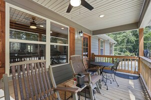 A covered outdoor deck with a table and chairs, a lantern, and a view of a house and trees.