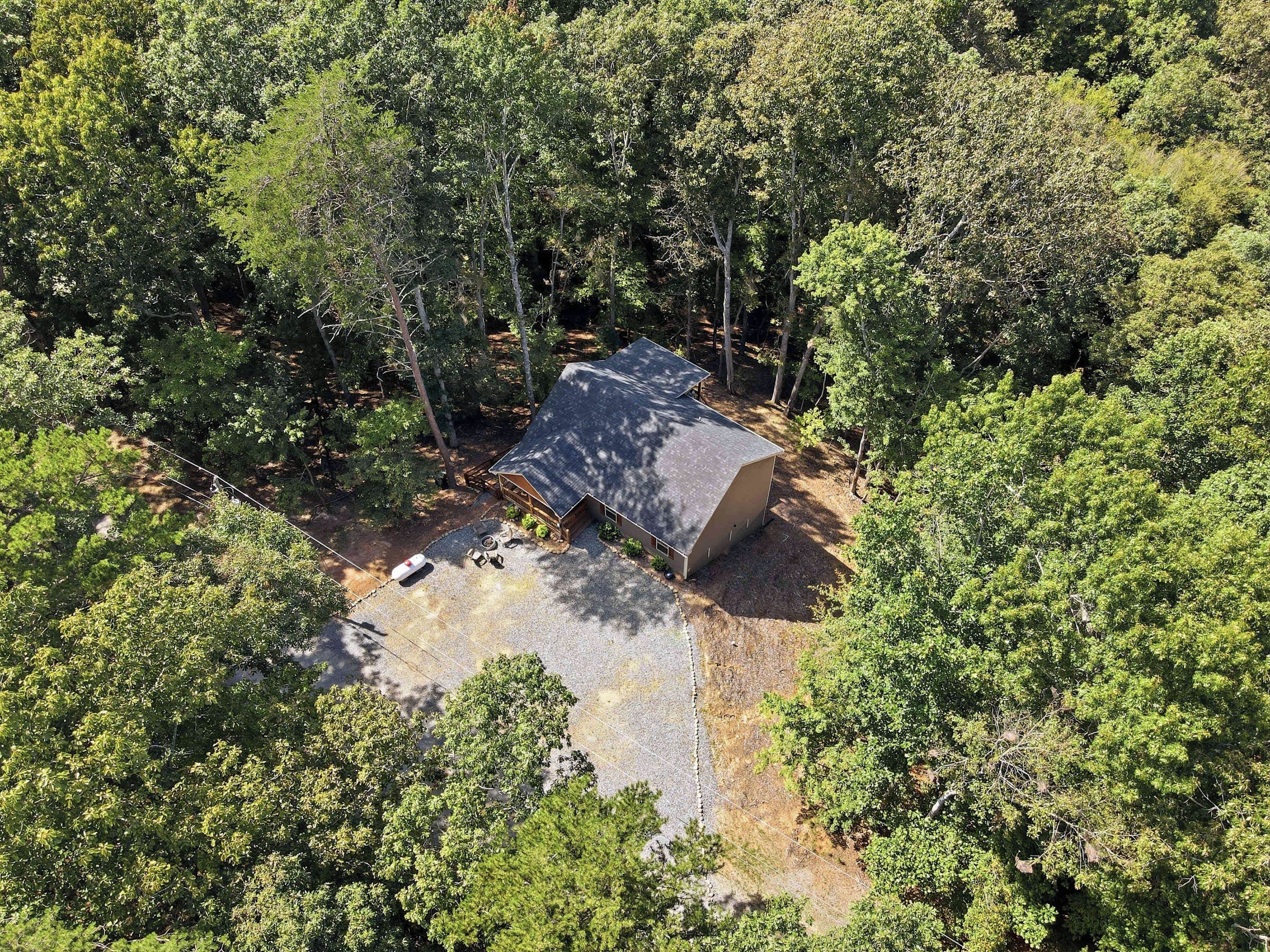 A secluded cabin surrounded by dense forest, with a gravel driveway and a small patio area.