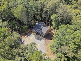 Una cabaña apartada rodeada de un bosque frondoso, con un camino de grava y una pequeña zona de patio.