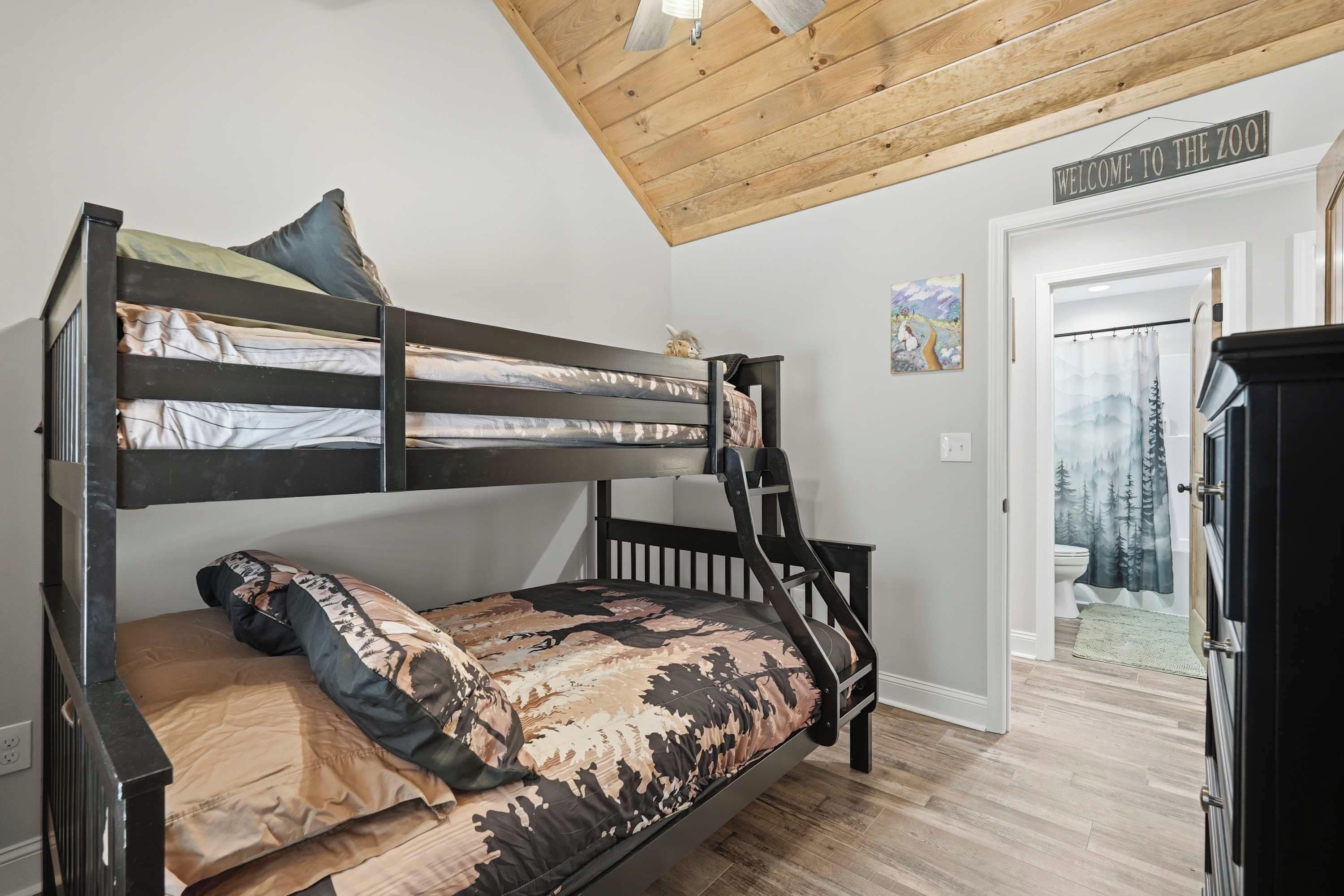 A bunk bed with a ladder, a door with a 'Welcome to the Zoo' sign, and a painting on the wall.