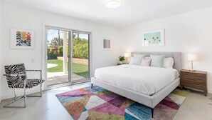 Une chambre à coucher avec un lit, une chaise, un tapis coloré et une porte-fenêtre coulissante donnant sur un jardin.