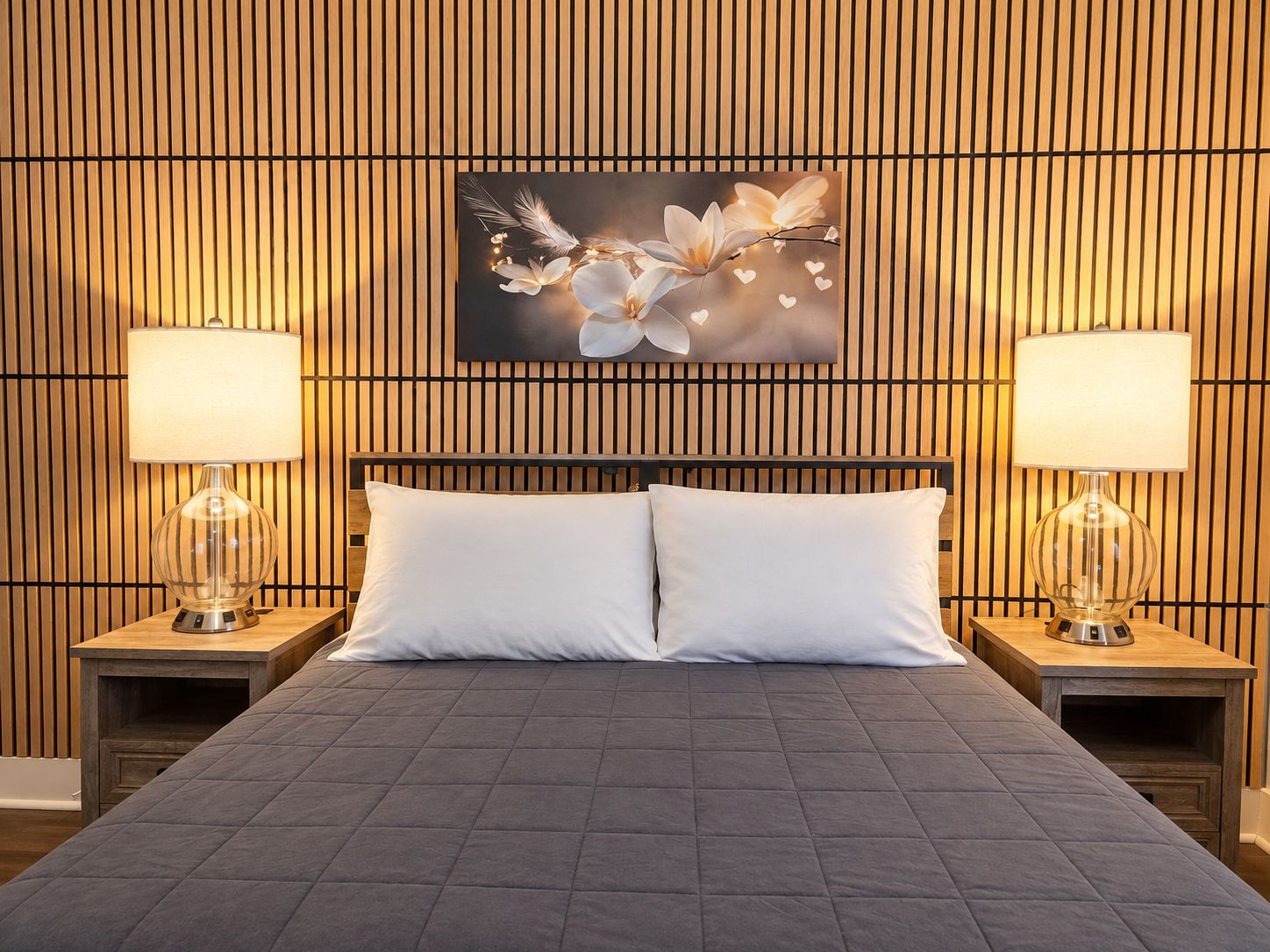 Une chambre d’hôtel comprenant un lit, deux tables de chevet avec lampes, une œuvre d’art accrochée au mur et un mur décoré de lattes de bois.