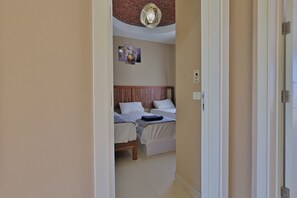 A narrow hallway leading to a bedroom with two beds, a wooden headboard, and a ceiling light fixture. - Seaview Villa, Pool, Bikes, Wi-Fi & Garden in Makadi Heights. Beach access (Hurghada)