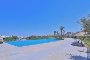Une piscine à l’eau d’un bleu cristallin, entourée d’une terrasse carrelée agrémentée de chaises longues et de palmiers.