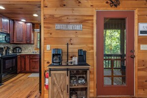Una cocina acogedora de estilo cabaña, con paredes de madera, una estación de café y una puerta que da a un balcón.