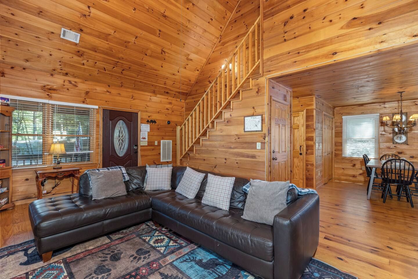 Un intérieur de chalet chaleureux avec un canapé d’angle en cuir, un escalier et un coin repas.