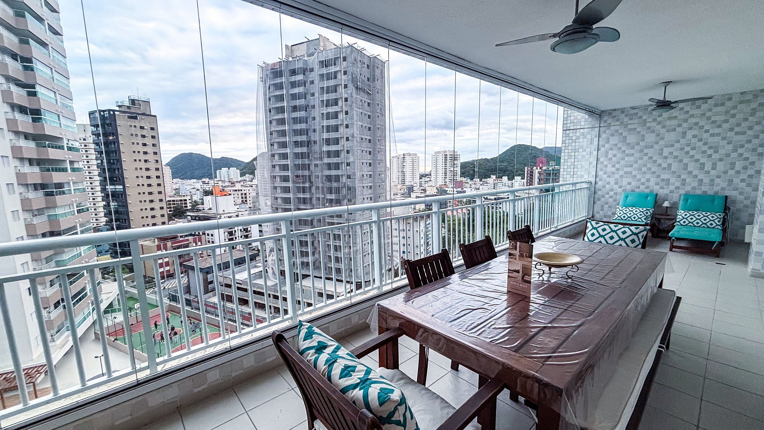 Un balcon avec une table à manger, des chaises et une vue sur un paysage urbain, avec des bâtiments et des montagnes.
