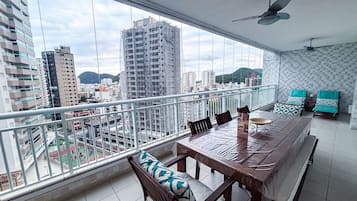 Uma varanda com mesa, cadeiras e vista para a paisagem urbana com edifícios e montanhas.