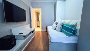 A narrow hallway with a bed on the right, a TV on the left, and a door leading to a bathroom.