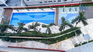 Zona de piscina al terrat amb diverses piscines, palmeres i un passeig tapat.