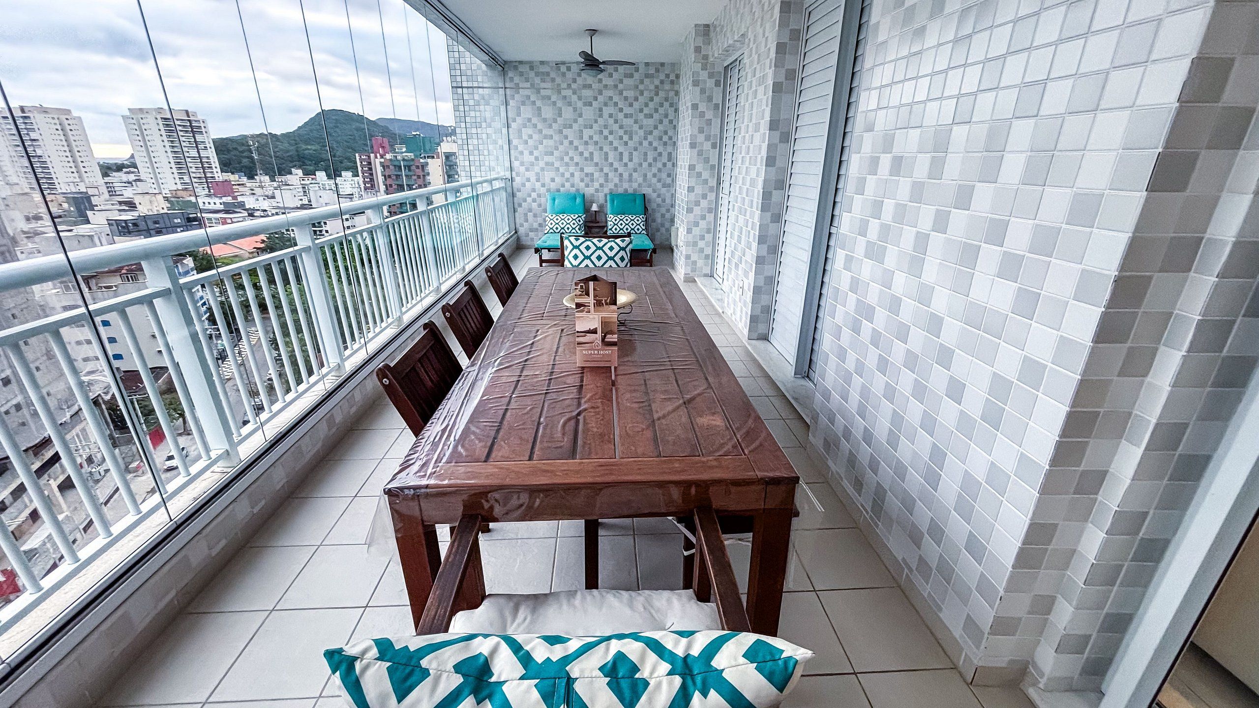 Un balcón con una mesa y sillas de madera, piso de baldosas y vista panorámica de la ciudad.